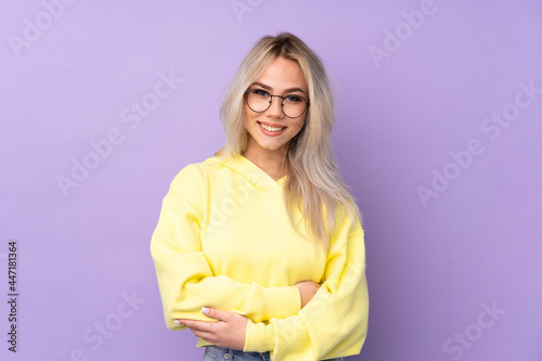 Teenager girl wearing a yellow sweatshirt over isolated purple background with glasses and smiling