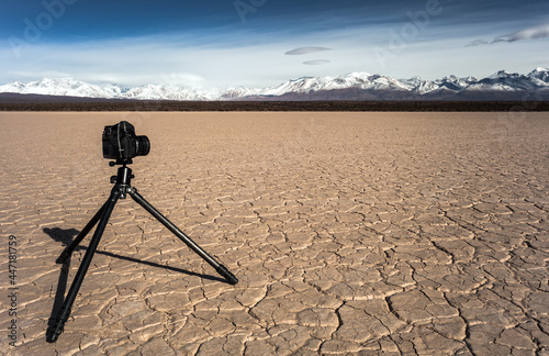 Εκτύπωση καμβά Film camera and tripod at the desert cracked dry earth and mountains background
