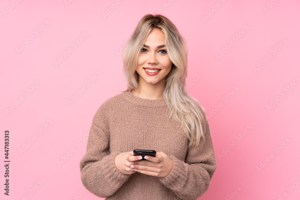 Teenager blonde girl wearing a sweater over isolated pink background sending a message with the mobile Teenager blonde girl wearing a sweater over isolated pink background sending a message with the mobile