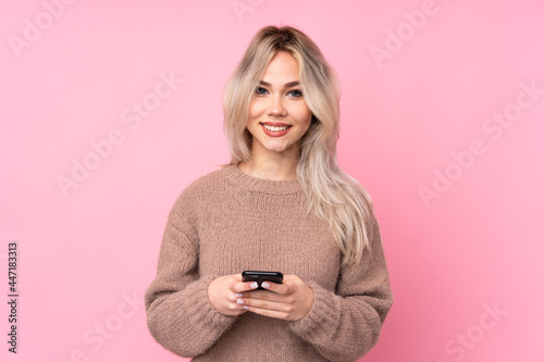 Teenager blonde girl wearing a sweater over isolated pink background sending a message with the mobile
