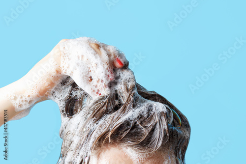 Girl washes her hair with shampoo on blue background, front view