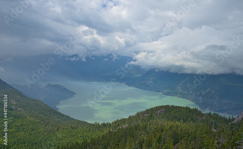 The lake surrounded by misty fog, mountains and forests is full of mystery. Aerial view from a cable car in Squamish, British Columbia, Canada. June 2019.