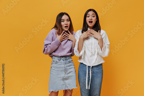 Brunette tanned Asian women look surprised on isolated orange background. Attractive girls pose in shock.