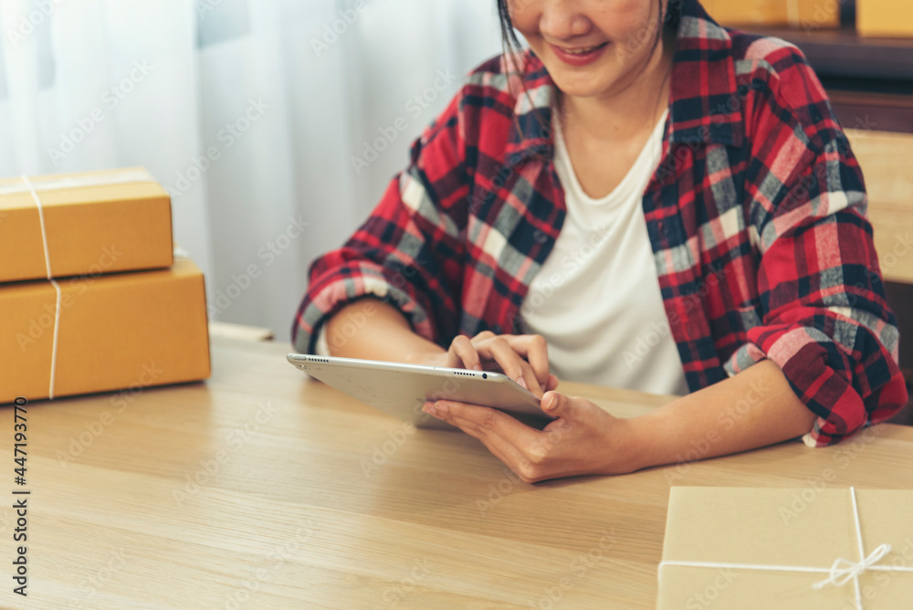 Asian woman startup small business at home office. Online seller entrepreneur young asian woman use tablet checking online order. Woman using tablet check stock goods supply delivery package shipping Asian woman startup small business at home office. Online seller entrepreneur young asian woman use tablet checking online order. Woman using tablet check stock goods supply delivery package shipping