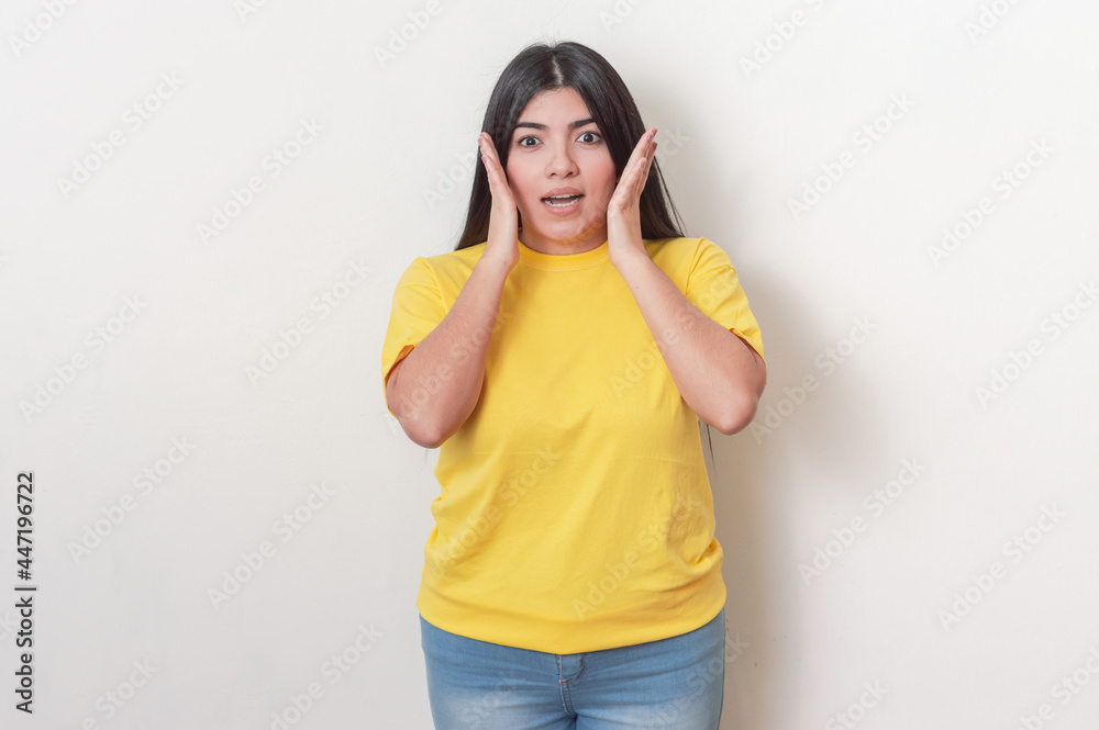 young white latin girl with black hair wearing yellow dress surprised with her hands on her face on a white background young white latin girl with black hair wearing yellow dress surprised with her hands on her face on a white background