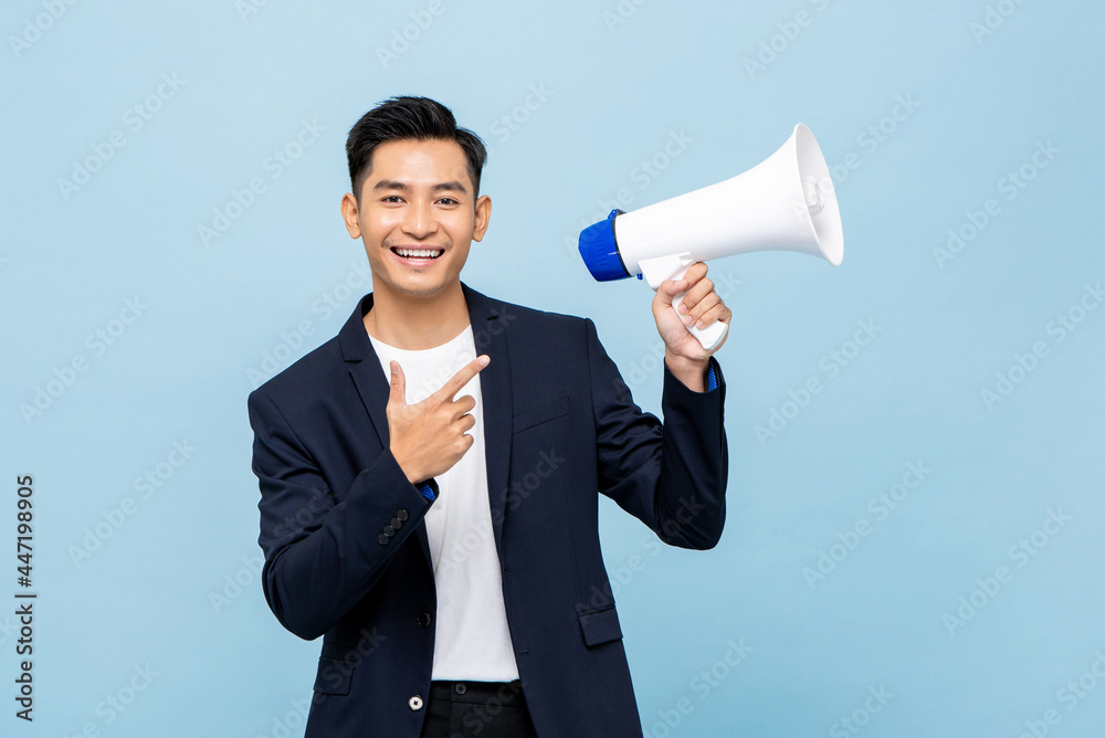 Smiling handsome Asian man holding megaphone in light blue isolated background Smiling handsome Asian man holding megaphone in light blue isolated background