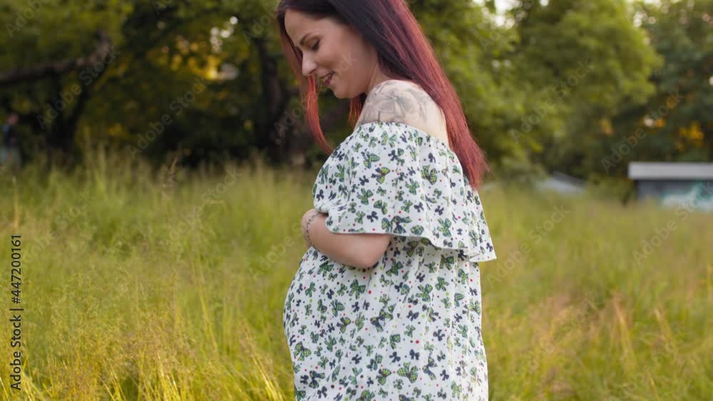 Side view of beautiful pregnant woman wearing stylish summer dress spending leisure time on nature. Smiling female touching tummy and enjoying happy moments. Woman at garden and hugging pregnant belly Side view of beautiful pregnant woman wearing stylish summer dress spending leisure time on nature. Smiling female touching tummy and enjoying happy moments. Woman at garden and hugging pregnant belly