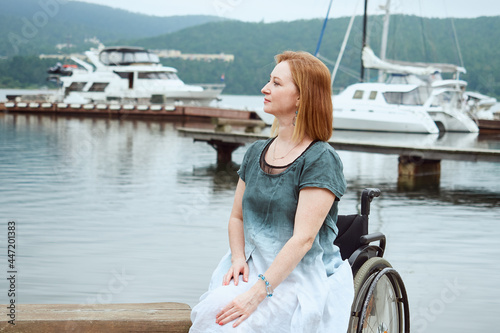 Portrait of a woman in a wheelchair on the background of a pier with catamarans © evafesenuk