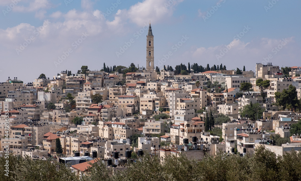 The exceptionally high bell tower of the main church, located in the Mount of Olives Ascension Monastery compound. Famous landmark of Jerusalem. The Arab village At-Tur on the foreground.