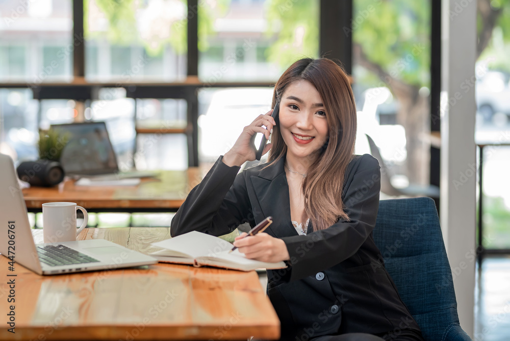 Asian businesswoman talking on the phone with taking notes put the laptop at the office. Looking at the camera. Asian businesswoman talking on the phone with taking notes put the laptop at the office. Looking at the camera.
