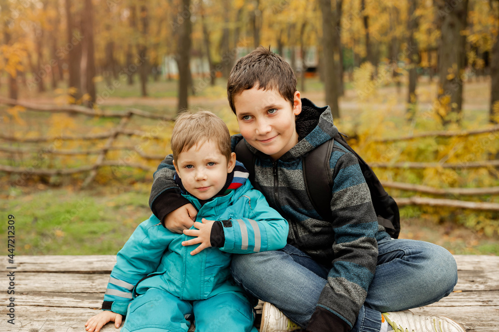 Two brothers play outdoors in autumn, best friends. Two happy boys in the woods. Cute brothers who are smiling happily together.Little brother with brother sit at the outdoor. Fraternal relations Two brothers play outdoors in autumn, best friends. Two happy boys in the woods. Cute brothers who are smiling happily together.Little brother with brother sit at the outdoor. Fraternal relations
