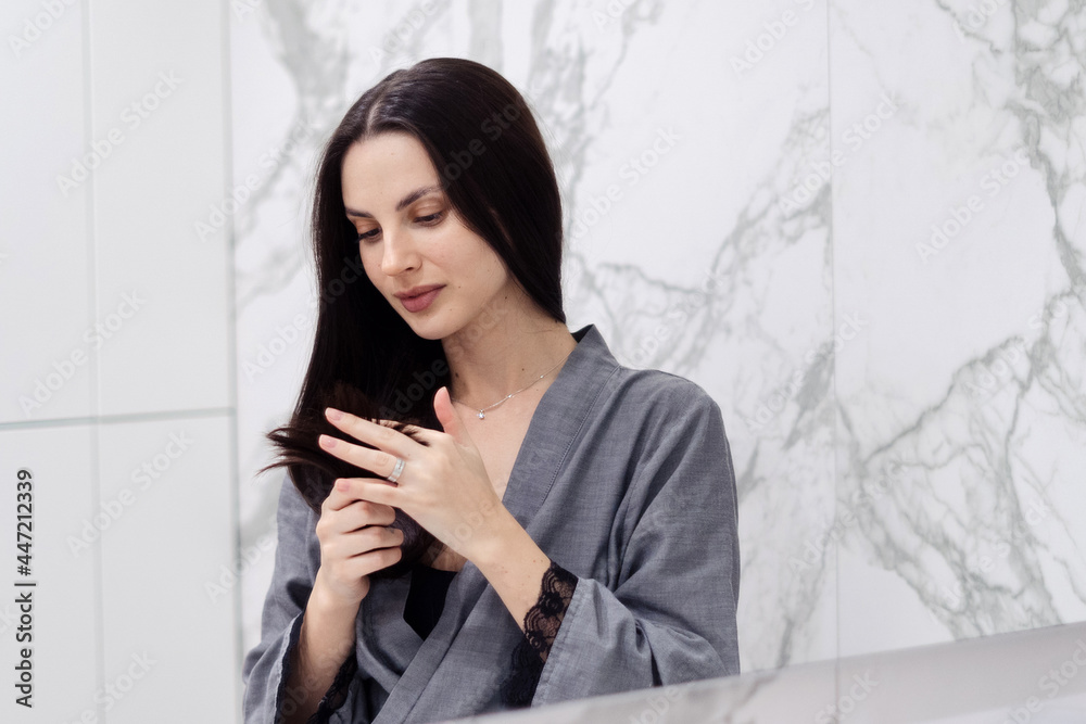 Brunette woman looking at hair ends in bathroom