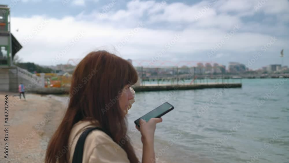 Pretty girl records a voice message on her smartphone. In the background, the seashore. Tilt and zoom shot. Slow motion. The concept of modern communication Pretty girl records a voice message on her smartphone. In the background, the seashore. Tilt and zoom shot. Slow motion. The concept of modern communication