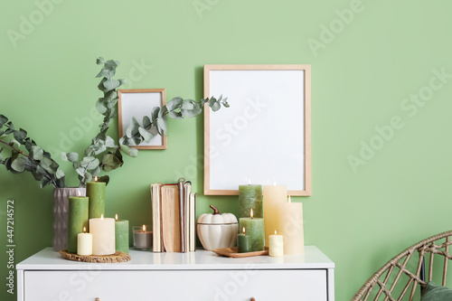 Burning candles and books on chest of drawers near color wall