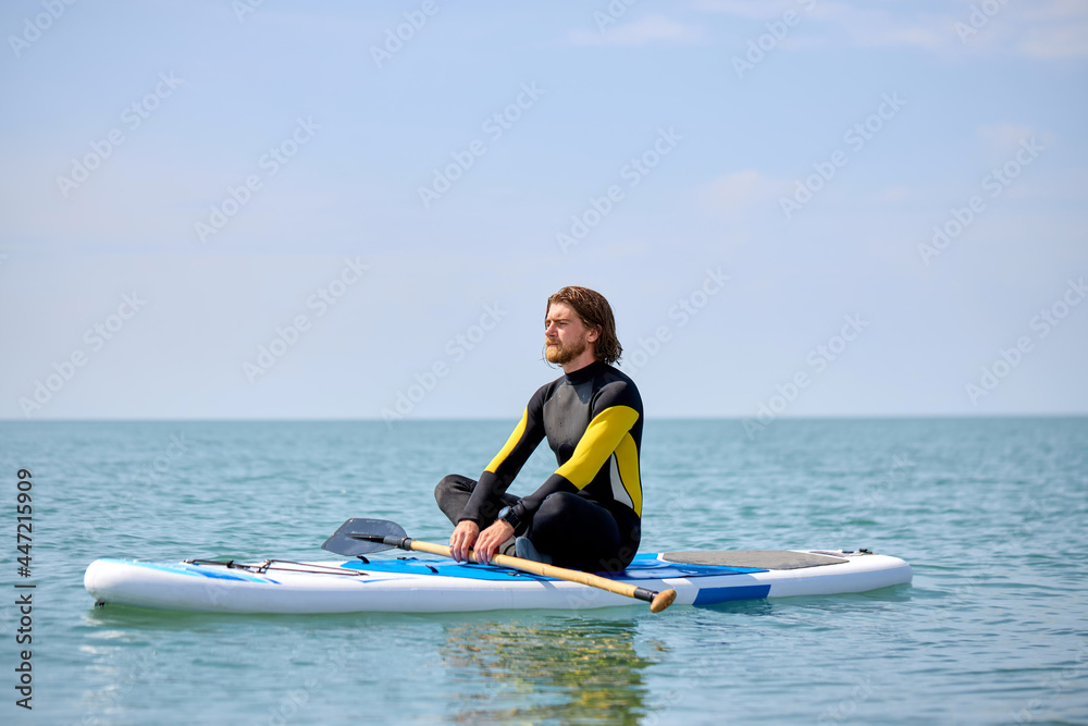 Athlete surfer mpractice yoga exercise on sup board at sea in relaxing day, meditating alone while sitting on surfing board, keep calm. yoga is meditation and healthy sport concept