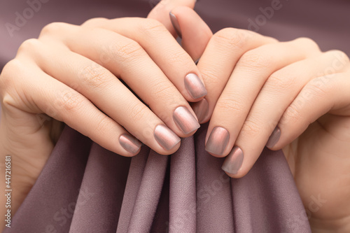Female hands with beige nail design. Glitter beige nail polish manicure. Woman hands hold brown fabric background. photo