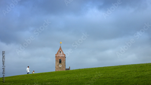 Walking the dog at the dike. Church tower and dike at Waddenzee coast at village Wierum Friesland Netherlands. 