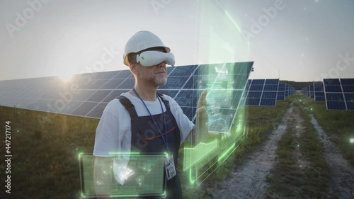 Adult male worker in VR glasses checking solar battery panels tapping online. 3D hologram graphic. Sunset sky. Futuristic technology innovation. Eco business trend. Virtual reality inspiration. 5G