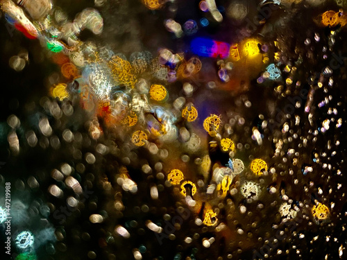 Shot through the glass in the rain with street lights and car headlights in the background. Blurred bokeh glitter of light background