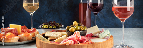 Italian antipasti or Spanish tapas panorama with wine, cold meat and cheese. Rose, white and red wine, a gourmet charcuterie and cheese platter and crostini with parma and salmon