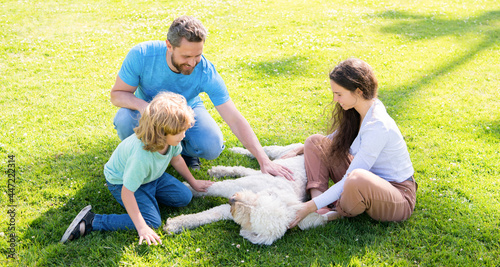 happy family of mom father and boy son playing with pet dog in summer park green grass, pet friendly