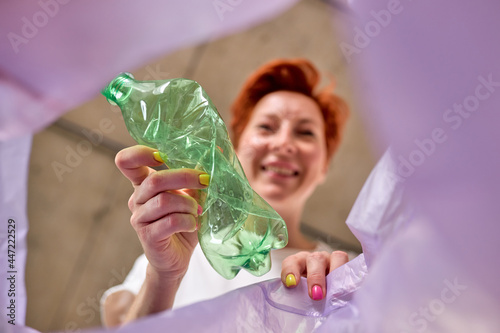 Slika na platnu Redhead caucasian Woman throws plastic bottle in trash, bottom view