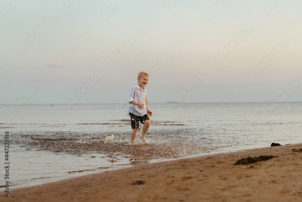handsome smiling caucasian boy wearing white shirt and shorts running from sea