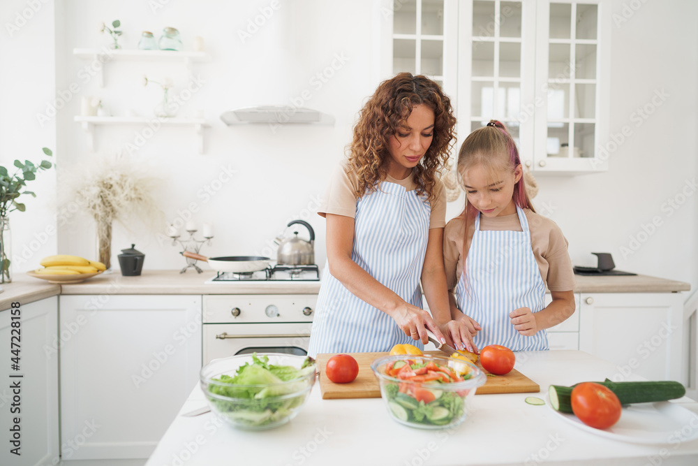 Mommy teaching her teen daughter to cook vegetable salad in kitchen
