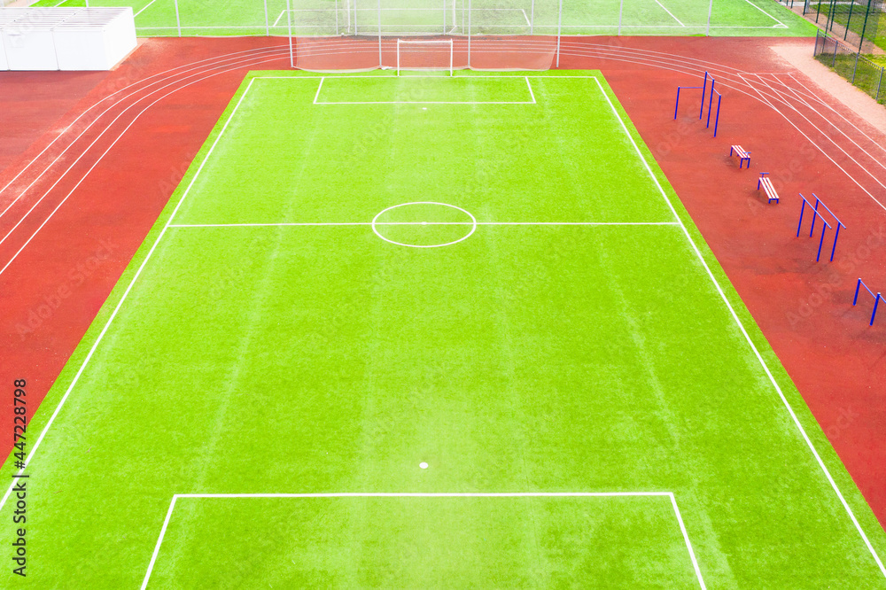 Obraz premium Football field with artificial turf and red running tracks, aerial view.