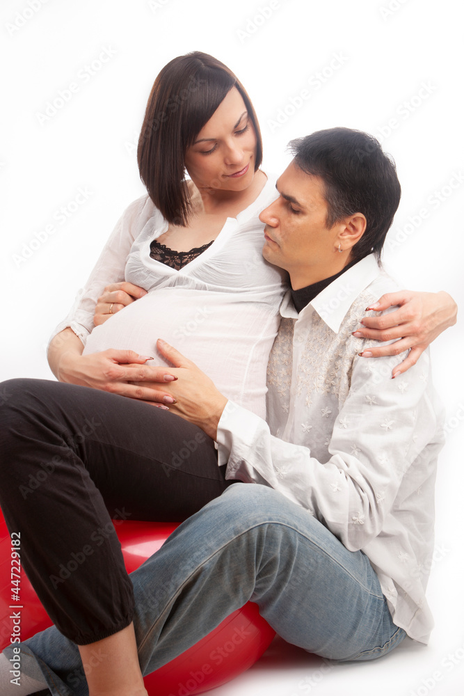 Portrait of Caucasian Man Together with Pregnant Wife Sitting On Fitball and Embracing Over White Background. Portrait of Caucasian Man Together with Pregnant Wife Sitting On Fitball and Embracing Over White Background.