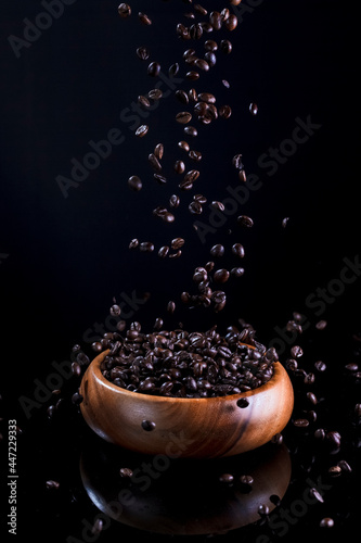 Food Concepts. Macro Image of Large Amount of Falling Fresh and Roasted Coffee Beans To Wooden Bowl Against Black Background.