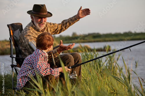 Foto Grandfather and kid boy together fishing in the evening at sunset time in summer
