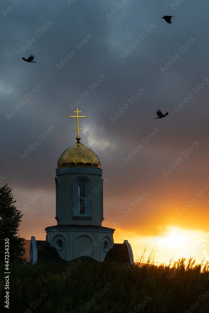 cross of the Orthodox chapel against the yellow sunset of the summer sun