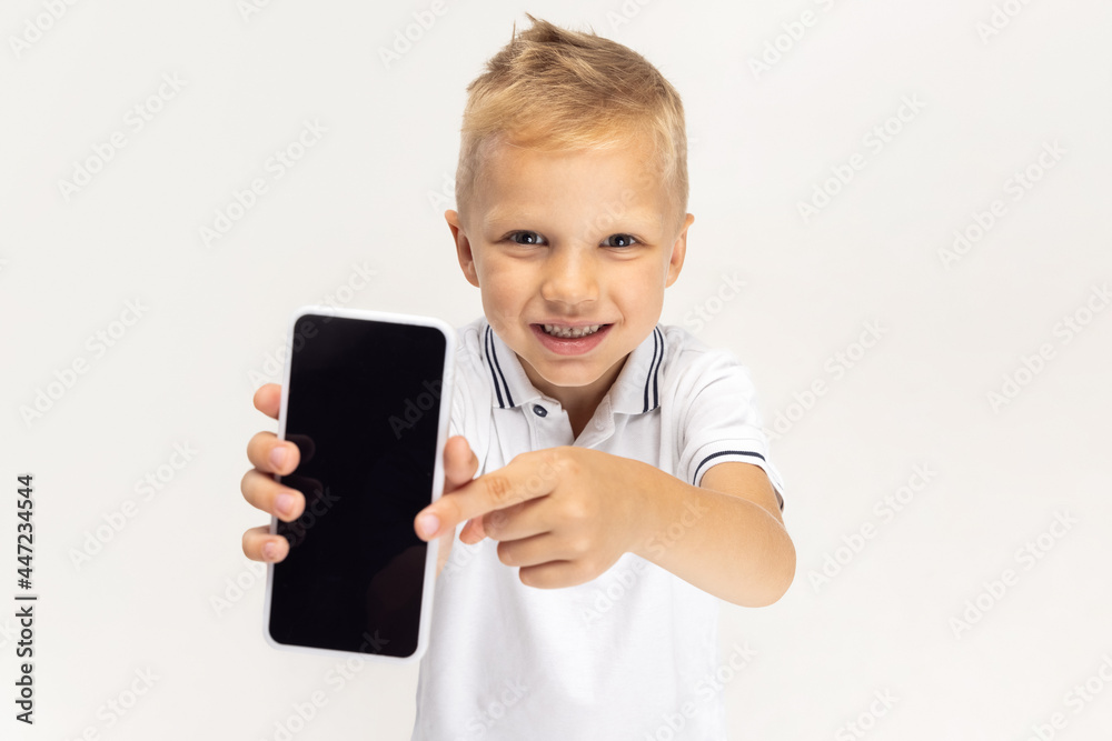 Close-up portrait of Caucasian preschool boy with phone isolated on white studio background. Copyspace for ad. Childhood, education, emotion concept