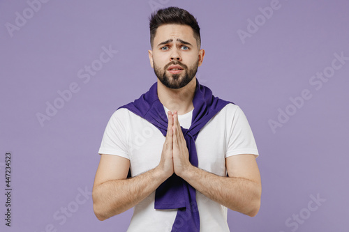 Attractive charming fashionable white young brunet man 20s wear white t-shirt purple shirt hands folded in prayer gesture, begging about something isolated on pastel violet background studio portrait