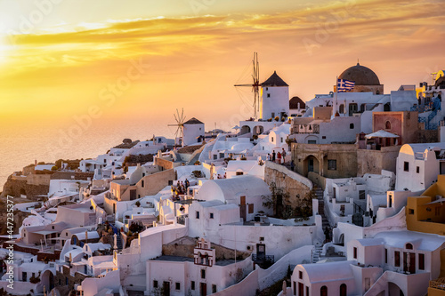 The windmills and whitewashed houses of Oia at Santorini island, Greece, during golden summer sunset time