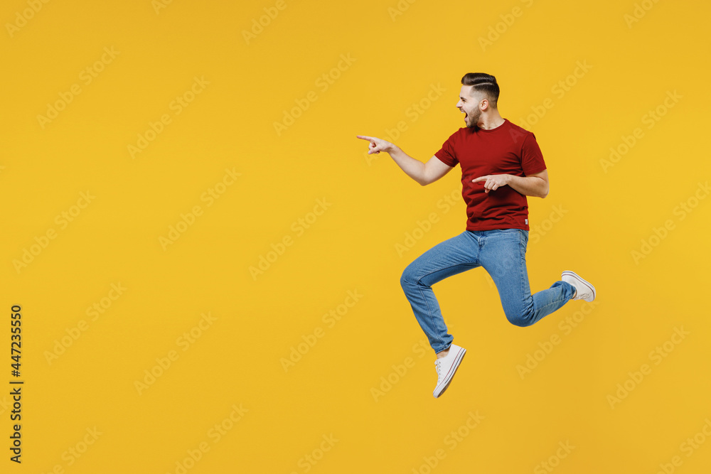 Full length excited young man in red t-shirt casual clothes jump high point index finger aside workspace area isolated on plain yellow color wall background studio portrait People lifestyle concept
