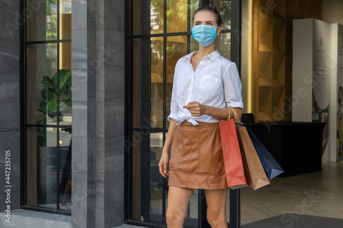 Beautiful woman wearing a mask to prevent COVID-19 and walking with colorful shopping bags out of a shopping mall.  © Supavadee