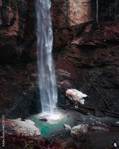 Beautiful mystic waterfall in autumn season. View on the stream falling down the cliff. Colorful giant cascade of water and person standing and watching at it.