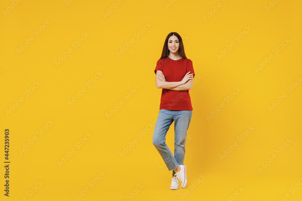 Full size body length excited smiling happy young brunette woman 20s wears basic red t-shirt stand hold hands crossed isolated on yellow background studio portrait. People emotions lifestyle concept. Full size body length excited smiling happy young brunette woman 20s wears basic red t-shirt stand hold hands crossed isolated on yellow background studio portrait. People emotions lifestyle concept.