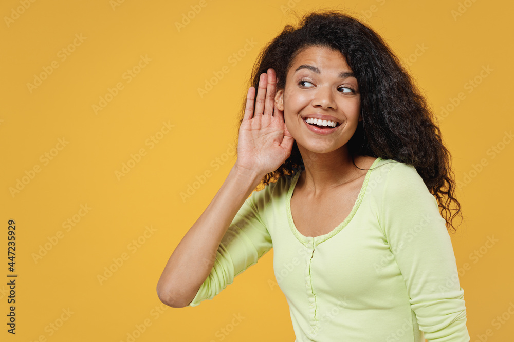 Curious nosy african american young brunette woman 20s wears green shirt try to hear you overhear listening intently isolated on yellow background studio portrait. People emotions lifestyle concept Curious nosy african american young brunette woman 20s wears green shirt try to hear you overhear listening intently isolated on yellow background studio portrait. People emotions lifestyle concept