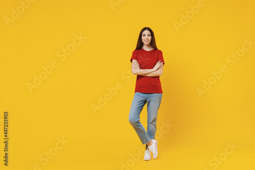 Full size body length excited smiling happy young brunette woman 20s wears basic red t-shirt stand hold hands crossed isolated on yellow background studio portrait. People emotions lifestyle concept. © ViDi Studio