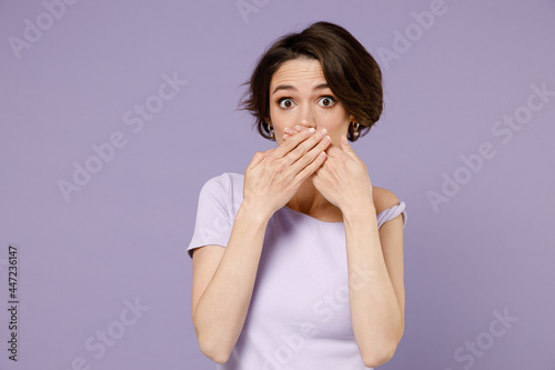 Young surprised shocked confused woman 20s with bob haircut wearing white t-shirt covering mouth with hands look camera isolated on pastel purple background studio portrait. People lifestyle concept