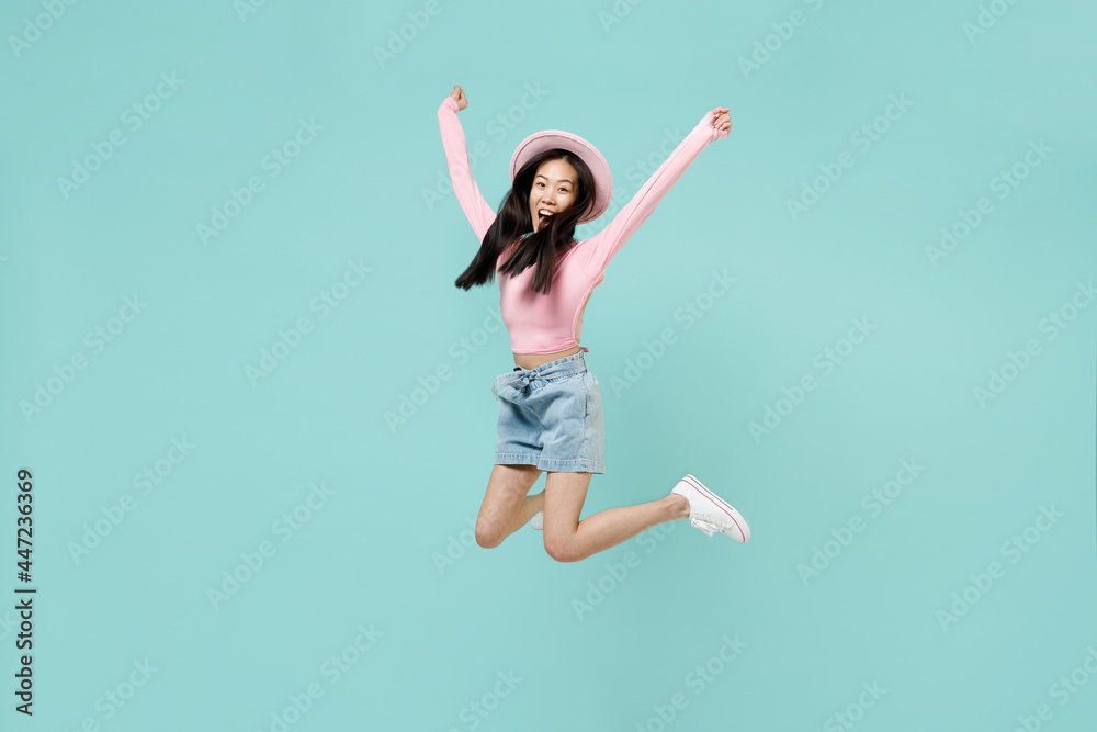 Full size body length overjoyed excited happy cheerful young brunette asian woman 20s with open mouth wear pink clothes jump raising her legs isolated on pastel blue color background studio portrait