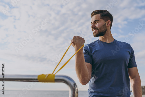 Youngn cool fun sporty strong fit sportsman man 20s in sports clothes warm up training with fitness rubber bands on handrail at sunrise over sea beach outdoor on pier seaside in summer day morning photo