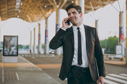 Traveler businessman happy man in black dinner suit stand outside at international airport terminal with attache case talk on mobile phone booking taxi order hotel Air flight business trip concept