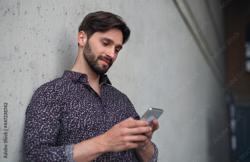 Fototapeta premium Portrait of young businessman standing indoors, using smarpthone.