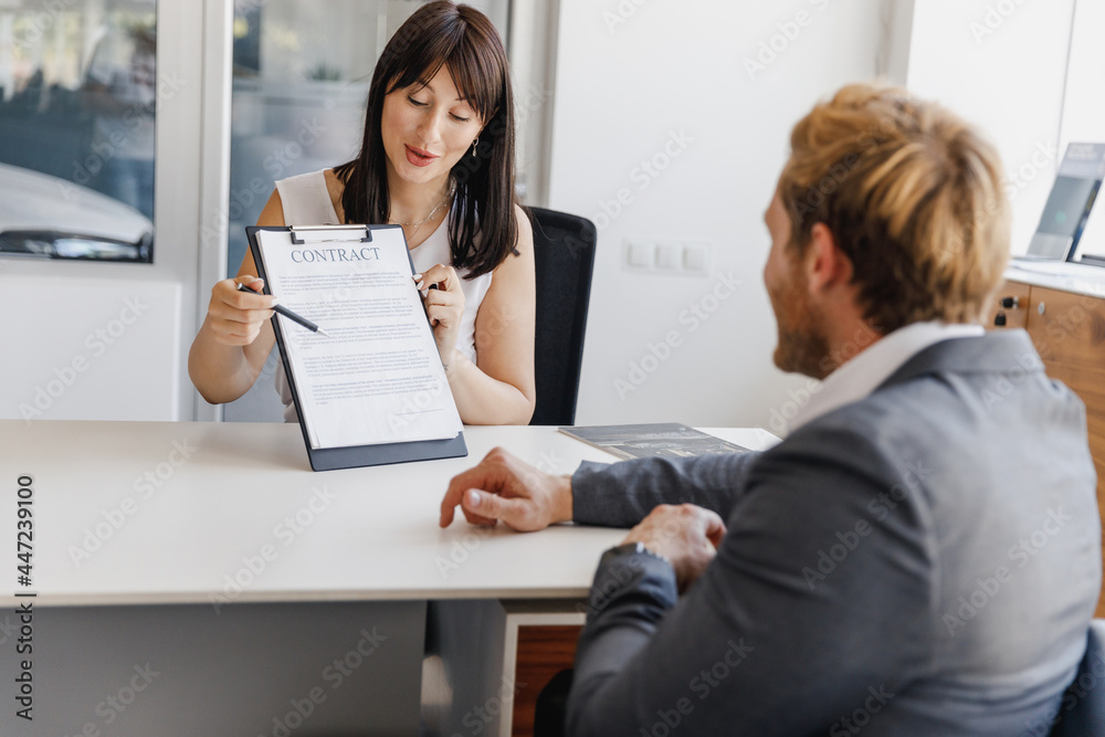 Man customer client male buyer in suit choose auto want buy new car automobile consult with salesman sign contract sitting at office in showroom salon dealership store motor show indoor Sale concept. Man customer client male buyer in suit choose auto want buy new car automobile consult with salesman sign contract sitting at office in showroom salon dealership store motor show indoor Sale concept.