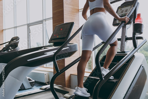 Cropped up photo shot back view young strong skinny sporty athletic sportswoman woman in white sportswear warm up train run on a treadmill climber stairs machine in gym indoor Workout sport concept. photo