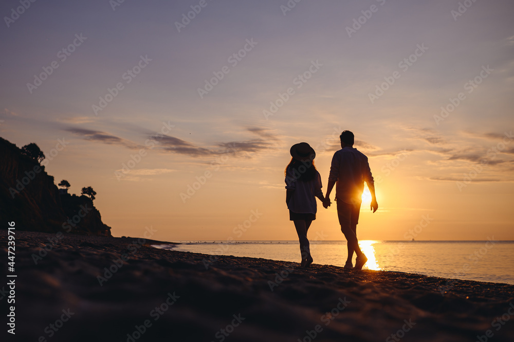 Full body back view silhouette young couple two friends family man woman in casual clothes hold hands walk stroll together at sunrise over sea beach ocean outdoor exotic seaside in summer day evening.
